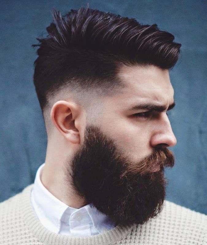 Side profile of a man with a textured drop fade haircut, spiked top, and a thick full beard.