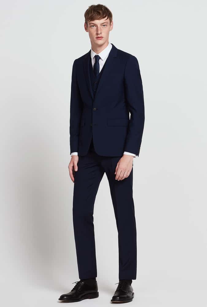 Man in a navy slim-fit suit with a white dress shirt and black formal shoes, showcasing a modern, minimalist formal look