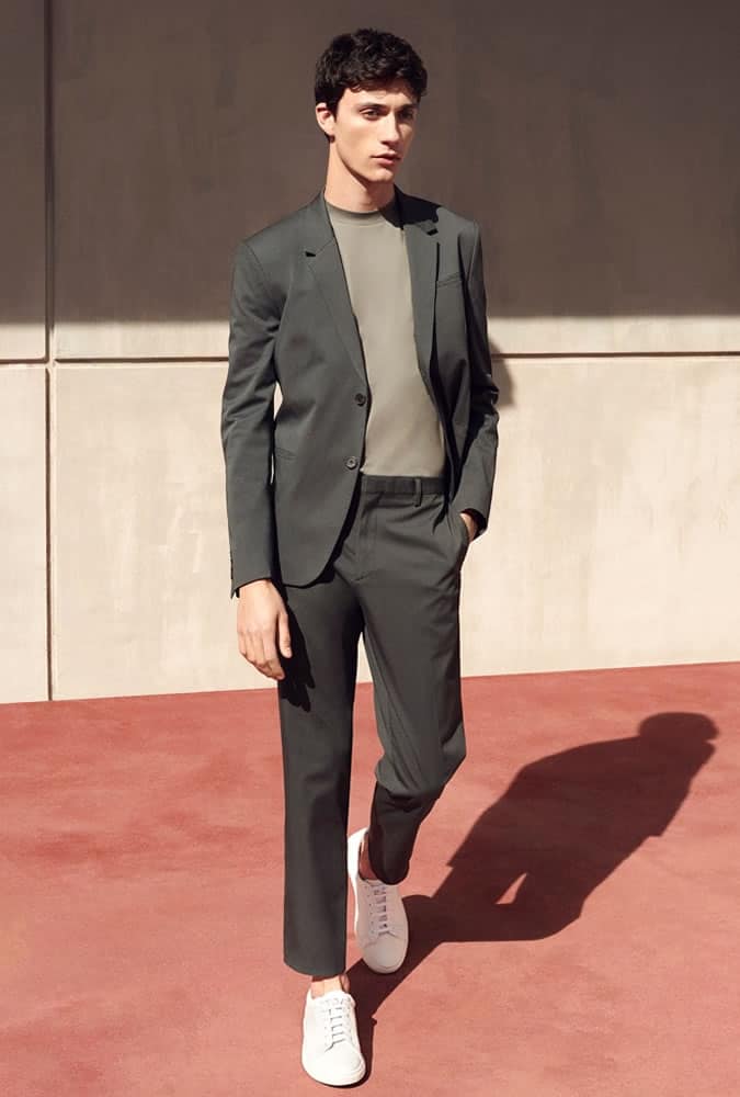 Man in a relaxed, modern gray suit with a light gray crew-neck shirt and white sneakers, demonstrating a casual yet sophisticated look