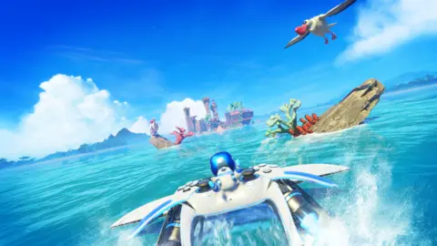 Sony Screenshot shows Astro Bot gripping onto an oversized PS5 controller equipped with rockets as it skims across the surface of a perfect blue tropical sea towards an island.