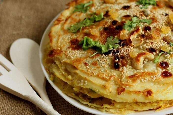 Chatti Pathiri, a layered Kerala dessert made with thin pastry sheets, sweet filling, and garnished with raisins, cashews, and sesame seeds.