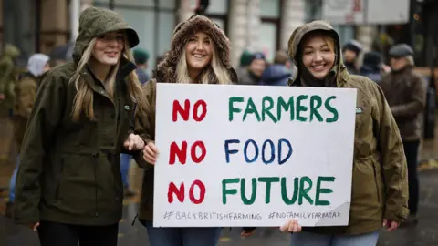 EPA Three women wearing coats with their hoods up in the rain hold a sign at the protest which reads 'no farmers, no food, no future'