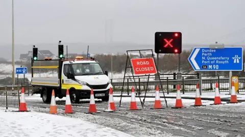 Reuters A row of traffic cones sit in front on a road closed sign. To the left is a blue motorway road sign showing the entrance to the M90 and the way to Dundee, Perth, North Queensferry and Rosyth.