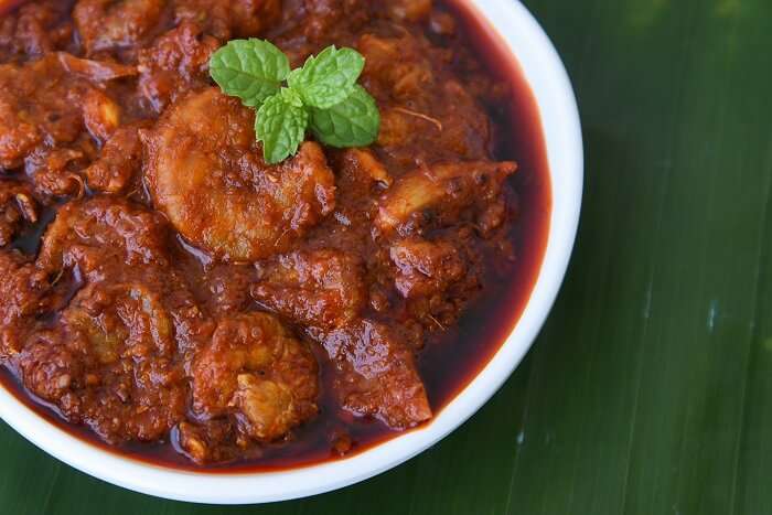 Kerala-style prawn curry with a rich red coconut-based gravy, garnished with fresh mint leaves in a white bowl