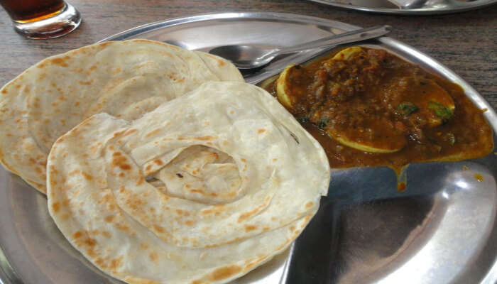 Malabar Parota, a flaky flatbread, served on a plate with a side of spicy curry.