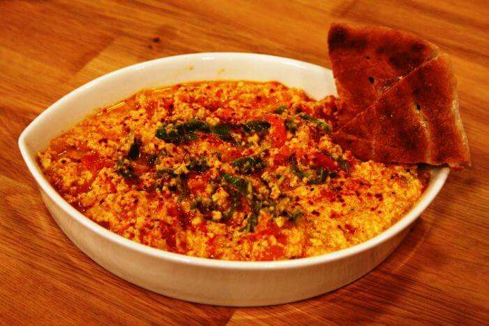 A bowl of traditional Turkish muhammara dip made with roasted red peppers, walnuts, and spices, served with bread.