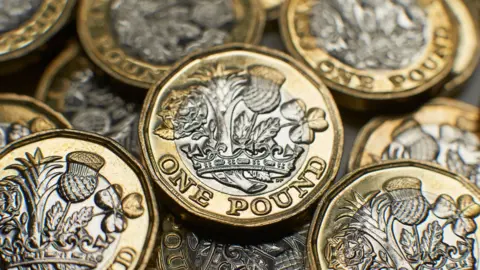 Getty Images A pile of one pound coins. They each feature a gold border with silver in the middle. An emblem is imprinted on them.