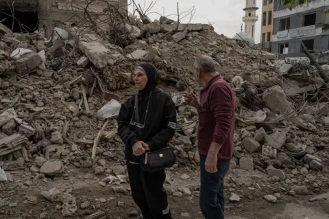 Niran Ali and her husdand stand in front of the remains of her destroyed children's clothing shop.