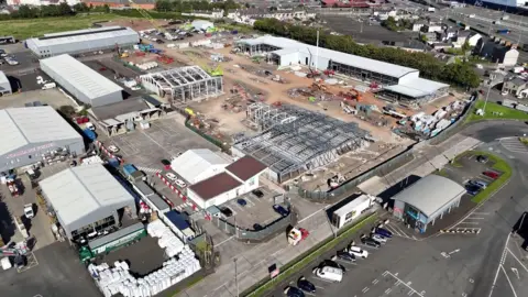 A drone image of an industrial shed being built. The steel frames have been put in place surrounded by lorries and diggers.