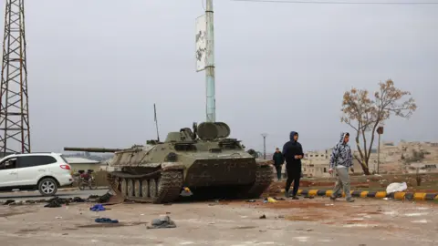 EPA People walk past a tank abandoned by Syrian troops after opposition fighters took control of the city of Hama, Syria, 07 December 2024. 