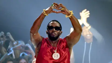 Getty Images Sean 'Diddy' Combs, pictured at the 2023 MTV Awards, holds his arms above his head and makes a "heart" symbol with his hands.