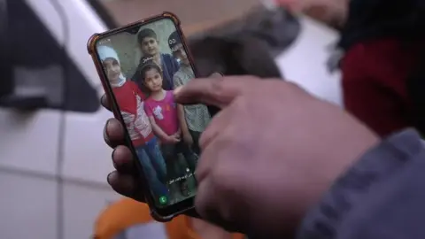 Tawfiq Diam points to a photo of his four children, on his mobile phone