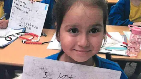 Surrey Police Sara smiling and looking directly at the camera. She is in a school classroom and holding a whiteboard. 