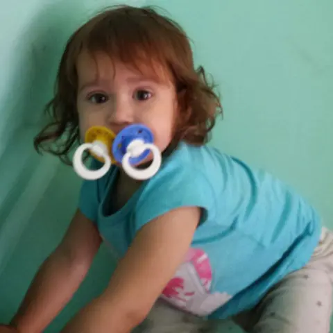 Sara Sharif picutred as a toddler with two dummies in her mouth, wearing a turquoise T-shirt and grey bottoms. 