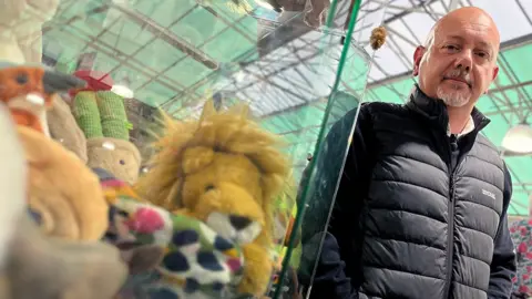 Chris Hoare, head of security at Old Barn Garden Centre in Sussex, stands in front of a glass cabinet inside which Jellycat soft toys are displayed.