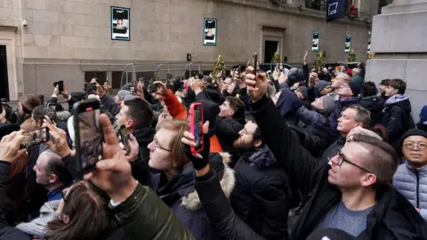 Reuters People crowded and in coats gather outside the NYSE with their phones in the air to watch US President-elect Donald Trump. Trump is not pictured, just a large packed crowd 