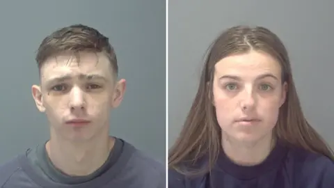 Suffolk Police Mugshots of Scott Jeff and Chelsea Gleason-Mitchell. Jeff is on the left, wearing a grey sweatshirt and looking directly at the camera. Gleason-Mitchell is on the right, wearing a navy sweatshirt and she has long brown hair.