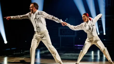 BBC/PA Chris McCausland and Dianne Buswell performing on Strictly in white suits
