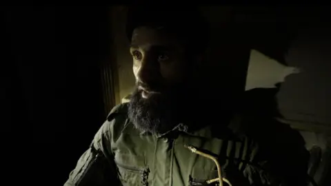 A photo of Abu Jarrah, face lit alone in the dark. 