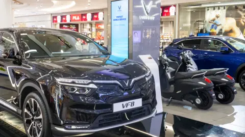 Getty Images A black car in a showroom with the letters VF8 on the number plate and two black scooters and a blue car in the background