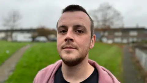 Marcus Johnson Marcus Johnson, 34, from Cwmbran, Torfaen, stands in front of some houses and a green.