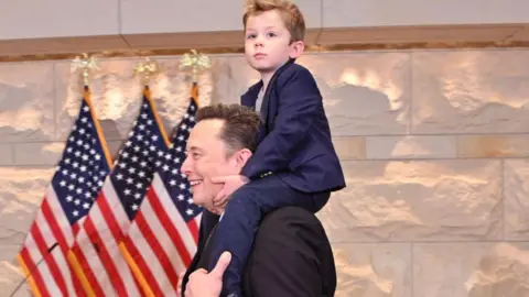 Getty Images Tesla CEO Elon Musk, co-chair of the newly created Department of Government Efficiency (DOGE), carries his son "X" on his shoulders before a meeting with members of Congress at the US Capitol  on 5 December 