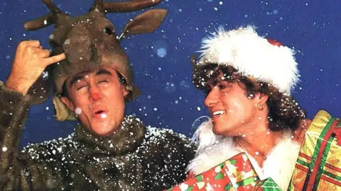 Sony Music Andrew Ridgeley dresses as a reindeer, while a Santa-hatted George Michael holds an armful of presents 