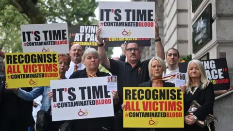 Getty Images Demonstrators outside the public inquiry in 2023 hold placards related to the infected blood scandal reading: "It's time" and "recognise all victims". 