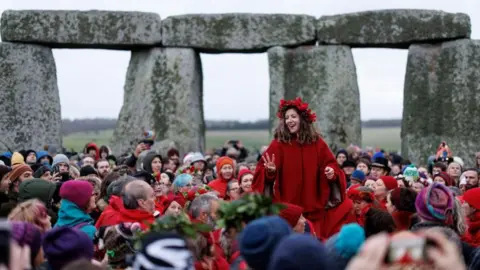 EPA Crowds of people inside Stonehenge and a woman dressed in red sitting on someone's shoulders in the foreground