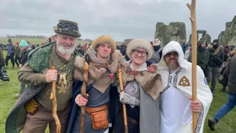 Four people carrying wooden staffs, dressed in druid clothing. Some have fur hats on