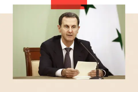 Getty Images Bashar al-Assad sits behind a microphone with papers in his hands, with a flag behind