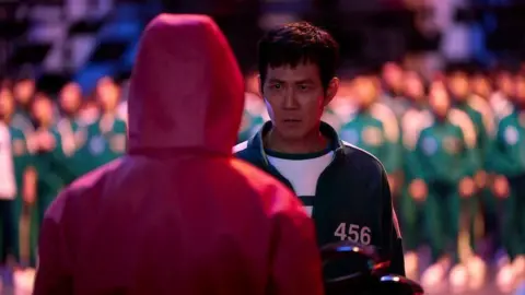 No Ju-han/Netflix Player 456 facing one of the guards in a pink hooded costume