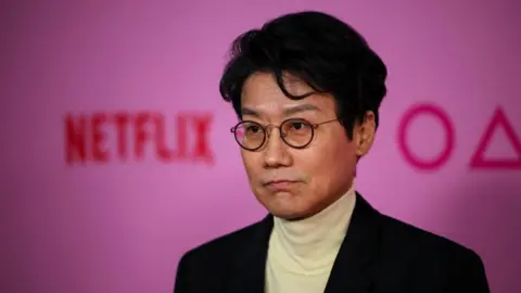 Reuters Director Hwang Dong-hyuk stands in front of a pink background with the words Squid Game and Netflix  at the premiere for Squid Game: Season 2, in Los Angeles, California, on December 12, 2024.