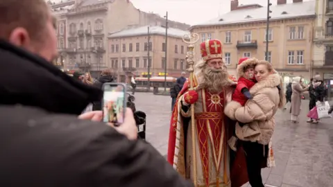 A woman and child are photographed next to a Ukrainian santa-like figure