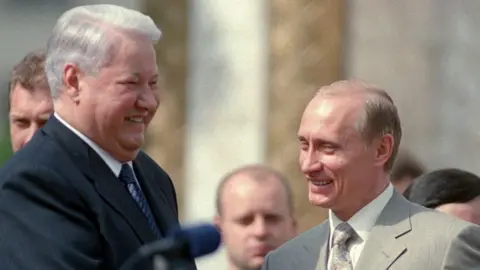 Getty Images A younger looking Vladimir Putin stands in front of Boris Yeltsin, both in suits and laughing