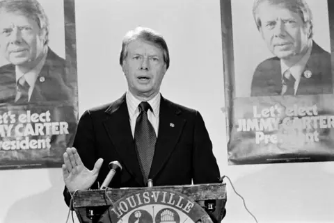 Getty Images  Then Governor of Georgia, Jimmy Carter stands in front of posters saying 'Let's Elect JIMMY CARTER President' and addresses the National Democratic Issues Convention, 23 November 1975