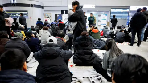 Reuters Relatives of passengers of the aircraft that crashed after it went off the runway are seated on the floor of the airport. 