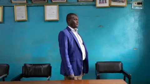 Kate Stanworth A man in a blue blazer stand in front of a turquoise wall