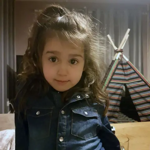 BBC Sara Sharif wearing a denim shirt standing in front of a play teepee