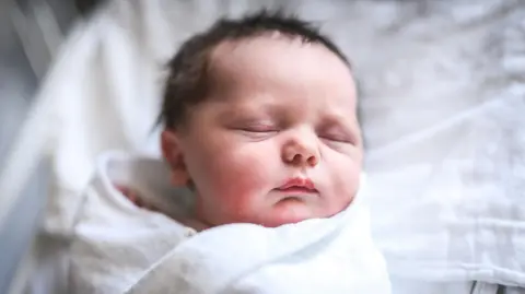 Getty Images A newborn baby with brown hair in a blankey