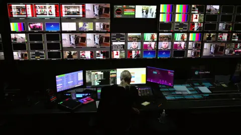 BBC A female director sits in front of a bank of screens inside a studio gallery at BBC Cymru Wales headquarters in Cardiff