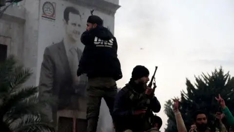 Getty Images Armed fighters in front of a banner depicting Assad in Hama