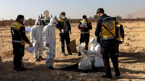 Getty Images White Helmets rescuers recover human remains from a mass grave near Baghdad Bridge, near Adra, north-west of Damascus. Photo: 17 December 2024