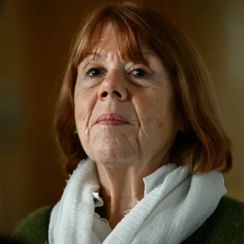 AFP A woman wearing a grey jacket and scarf looks directly at the camera expressionless.