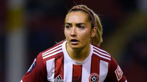 PA Media A woman with a blonde ponytail wearing a red and white striped Sheffield United kit plays football.