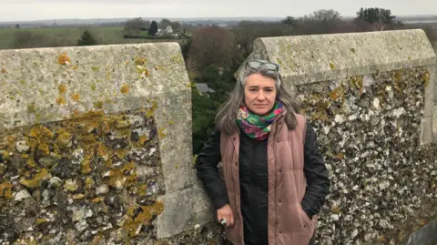 BBC Monique Bonney in front of a stone wall. Behind her is a view of north Kent, including fields, a house and in the distance a town. 