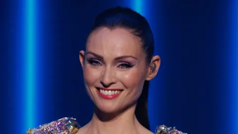 BBC STUDIOS/ANDY HEATHCOTE Sophie Ellis Bextor at her New Year's Eve Disco concert for BBC One, she is smiling and has her dark hair scraped back in a high ponytail