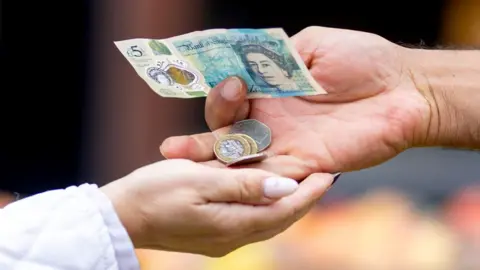 Getty Images A person's hand gives change to another person's hand, including a £5 note and coins