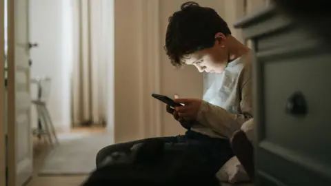 Getty Images A boy sits on the floor looking at his smartphone.