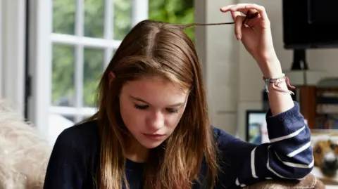 Getty Images A girl twiddles a lock of hair while looking at her iPhone